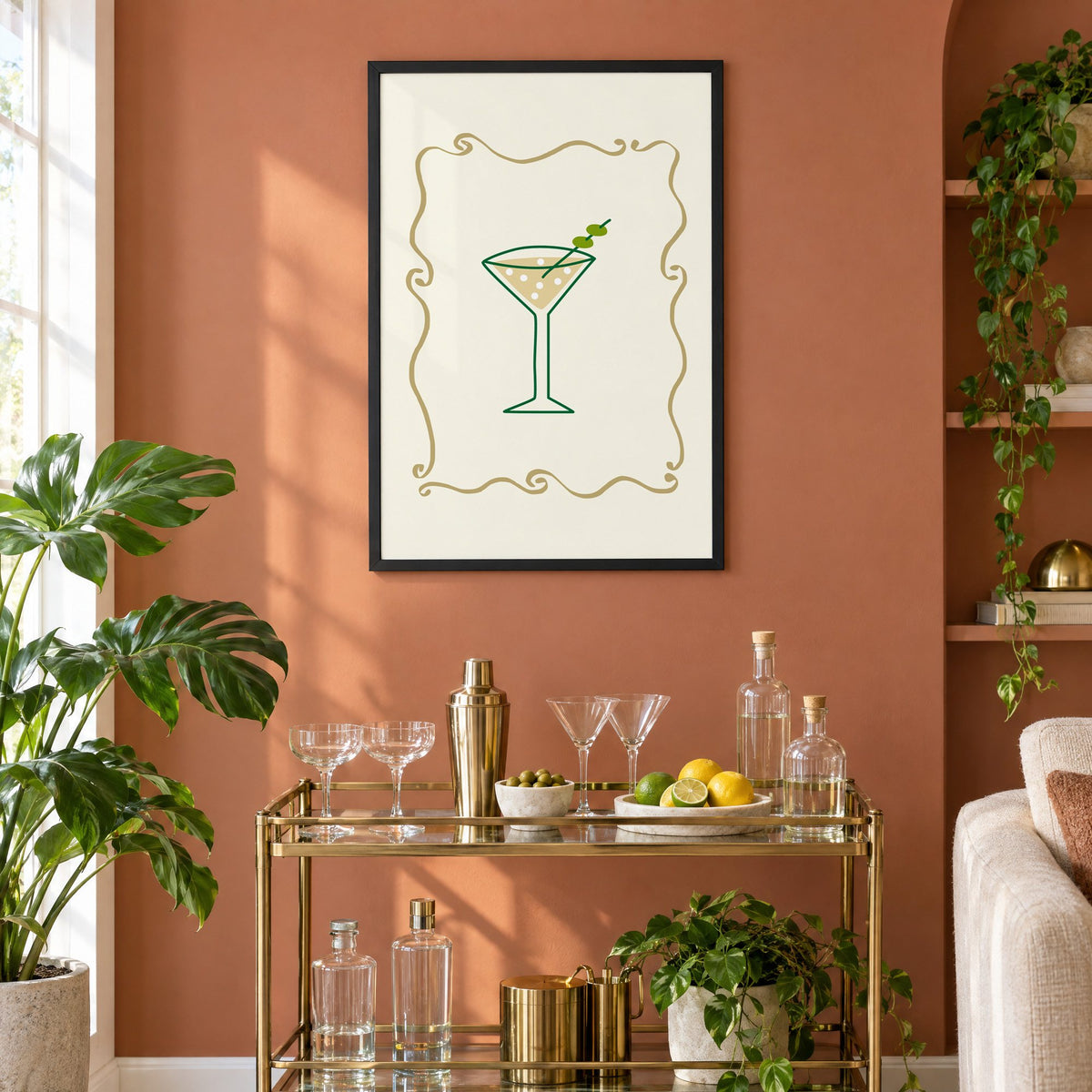 Olive martini in gold scroll frame print in a black frame on a terracotta wall above a brass bar cart with coupes and citrus