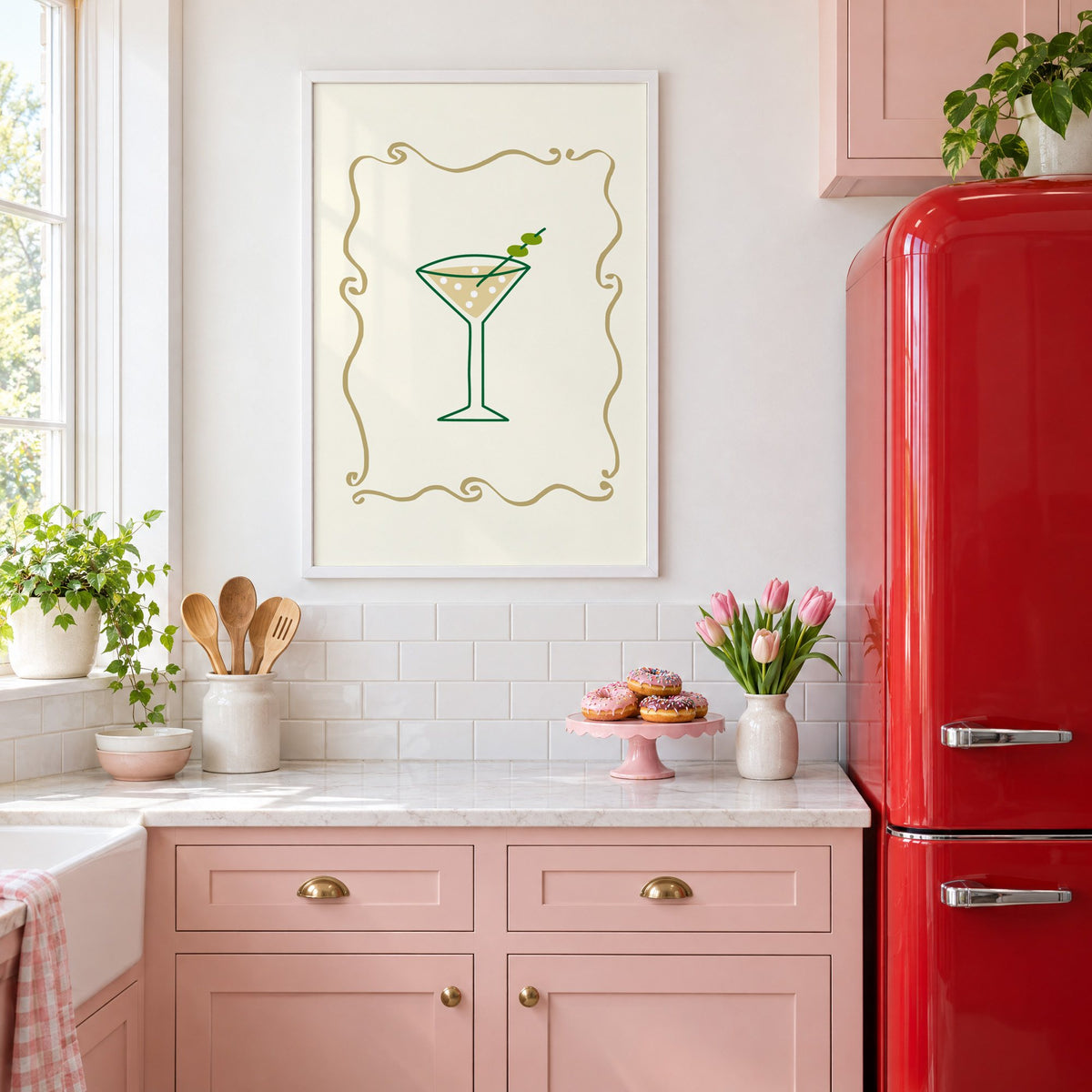 Olive martini in gold scroll frame print in a white frame above pink cabinets beside a red retro fridge