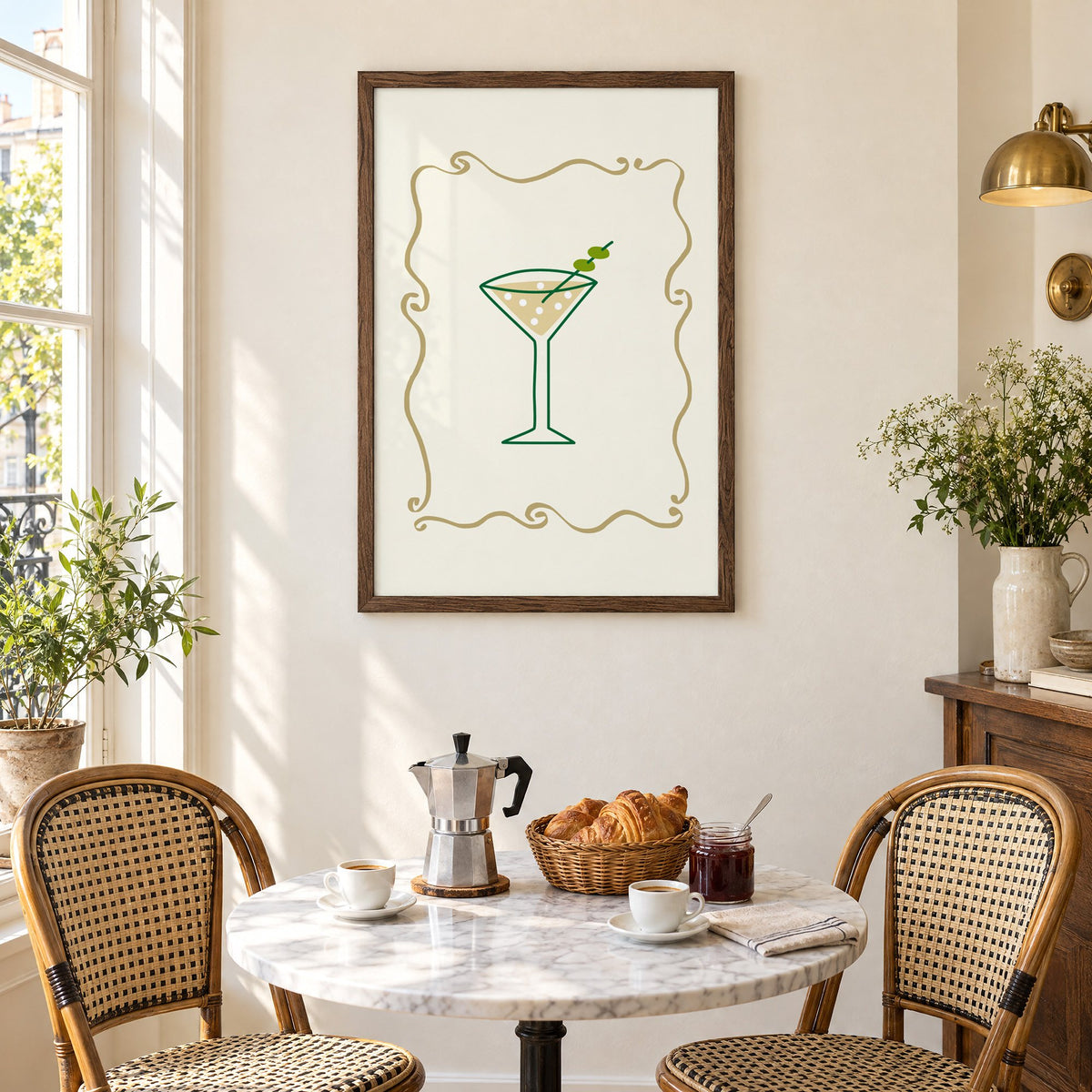 Olive martini in gold scroll frame print in a walnut frame above a marble bistro table with croissants and rattan chairs