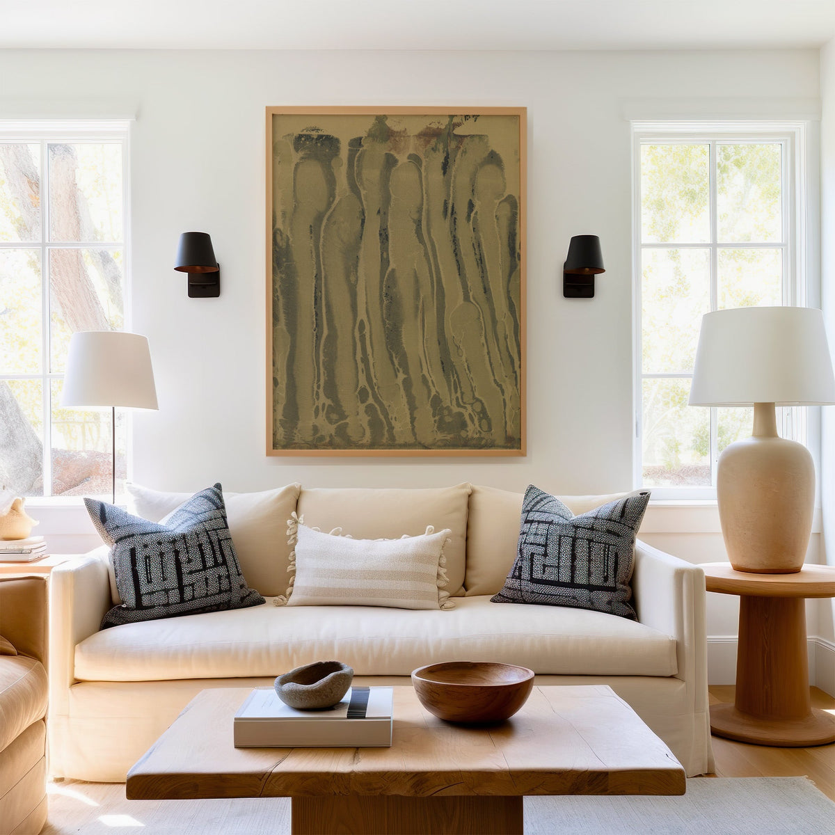 Olive and sepia marbled ink drips print in a light oak frame above a cream sofa between two black wall sconces