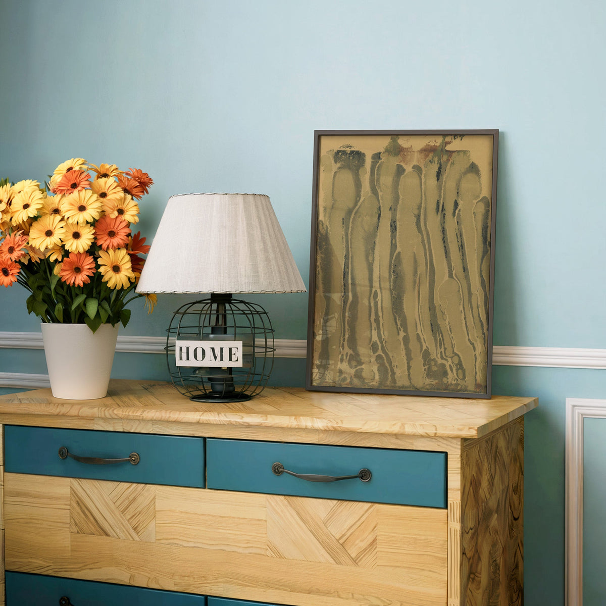 Olive and sepia marbled ink drips print in a charcoal frame on a teal dresser beside orange and yellow daisies