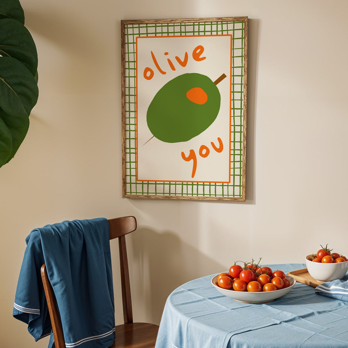 Olive you green olive print in an oak frame above a blue linen table with ripe tomatoes