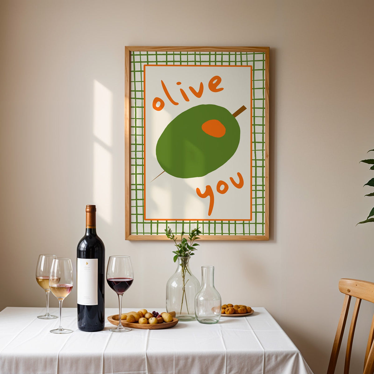 Olive you green olive print in an oak frame above a table laid with red wine and glasses