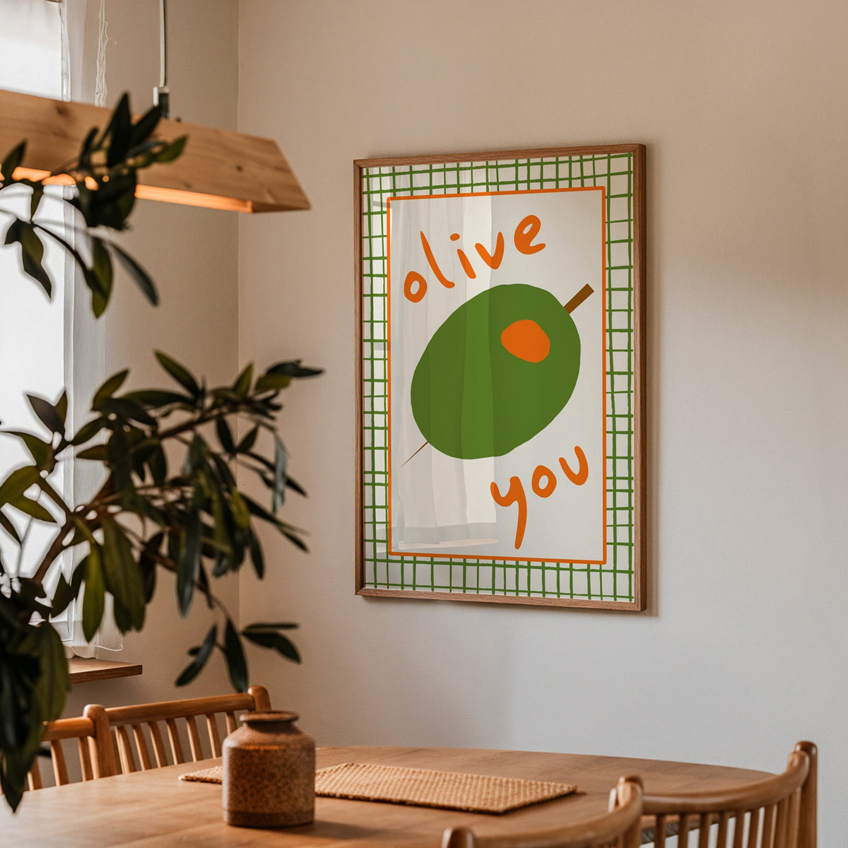 Olive you green olive print in a walnut frame above a dining table beside an olive tree