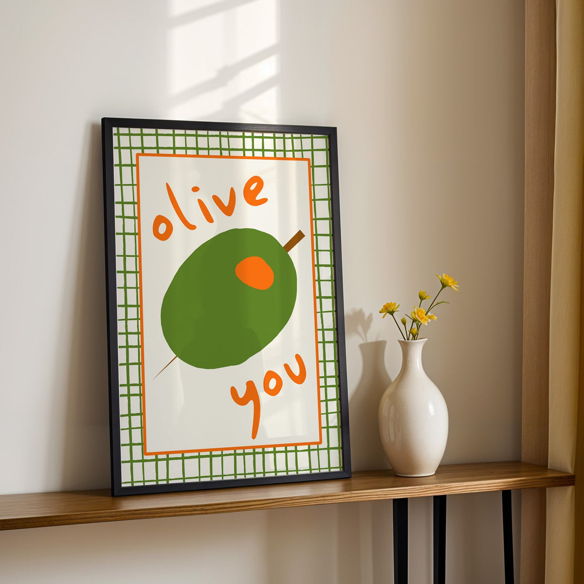 Olive you green olive print in a black frame on a console table with yellow daisies