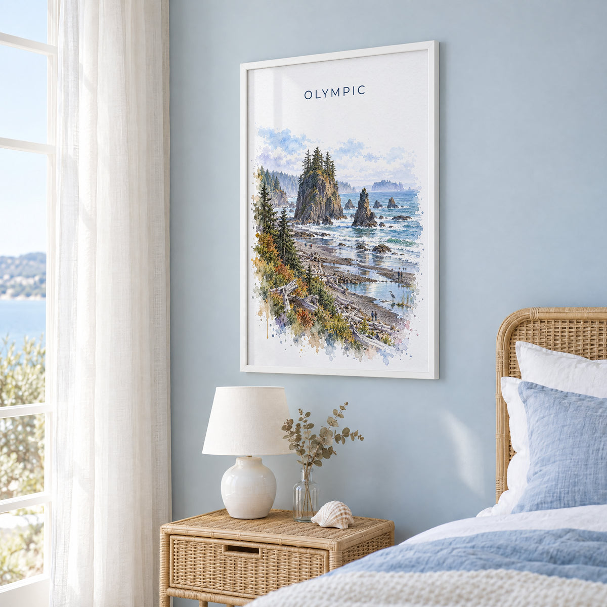 Olympic National Park watercolor print in a white frame on a pale blue wall beside a rattan bed in a coastal bedroom