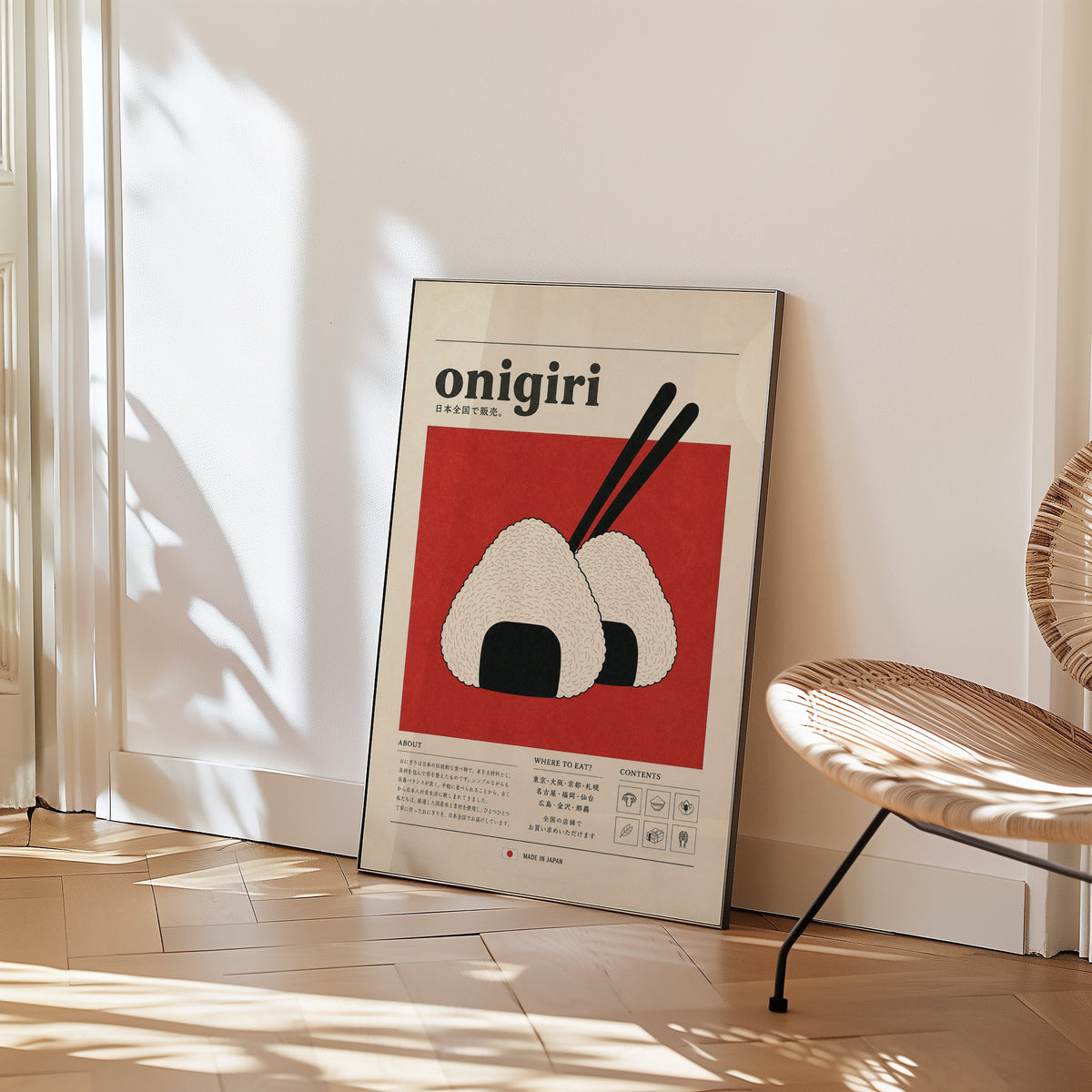 onigiri rice balls on red print in a black frame leaning on a herringbone floor beside a woven rattan chair