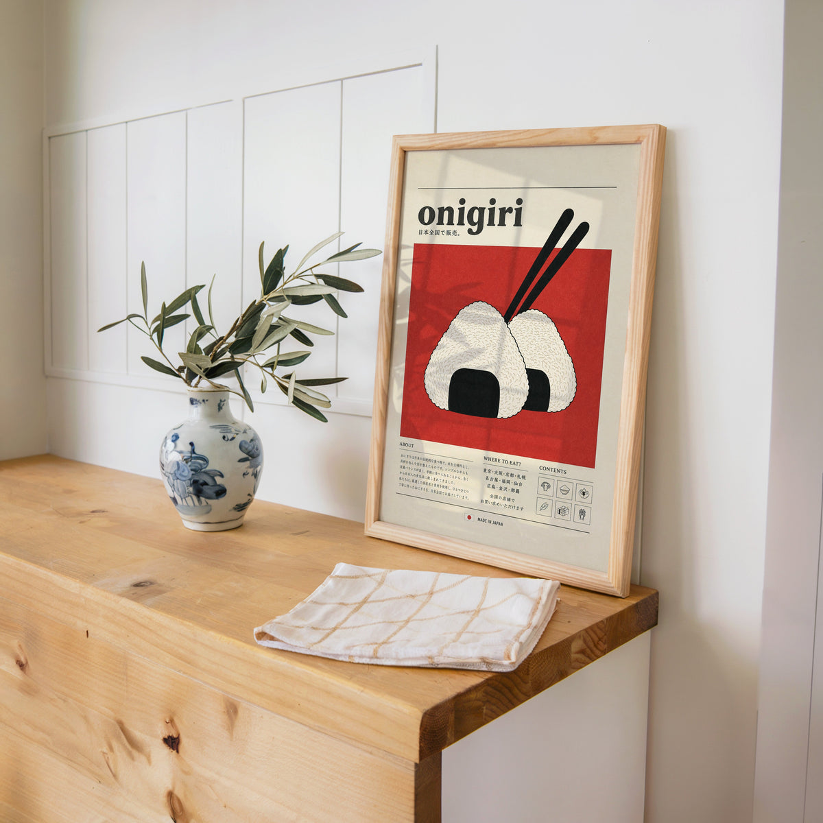 onigiri rice balls on red print in a pine frame on a wooden counter beside a blue and white porcelain vase