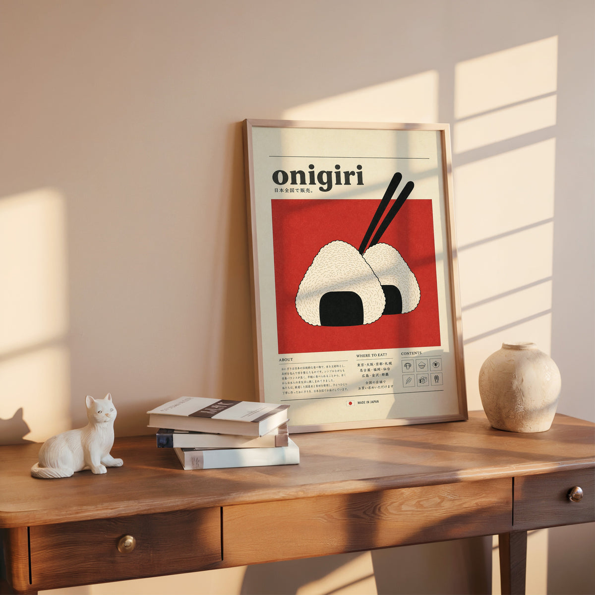 onigiri rice balls on red print shown in a rose gold frame leaning on a wooden writing desk with books