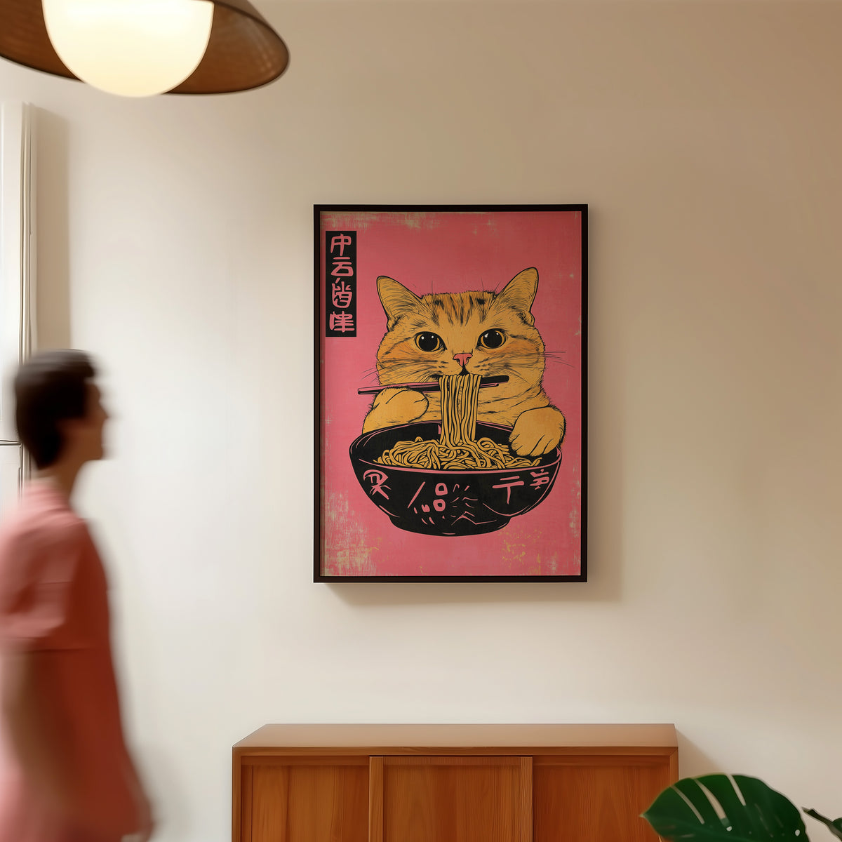 Orange tabby cat slurping ramen print in a black frame in a hallway under a rattan pendant
