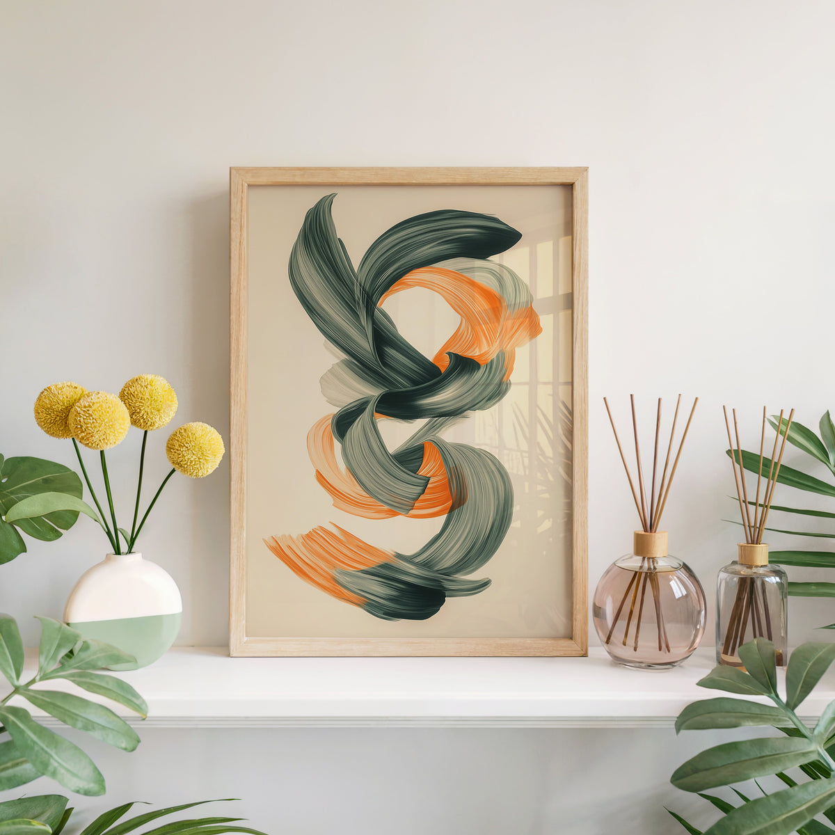 Orange and green brushstroke knot abstract print in a light oak frame leaning on a white mantel with yellow flowers