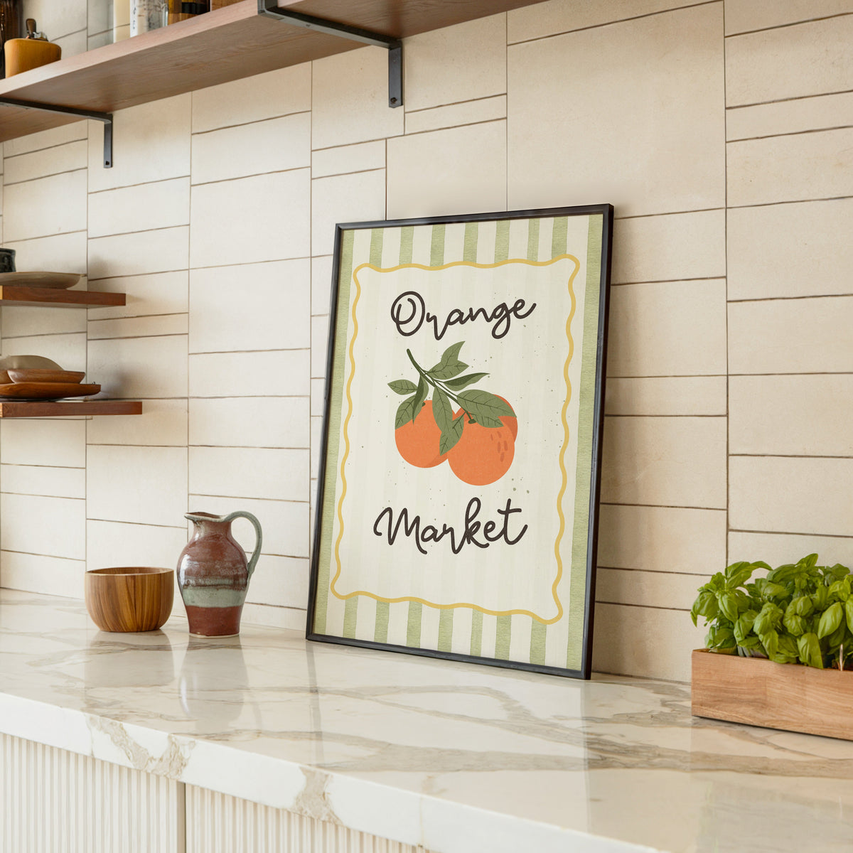 Orange Market print in a black frame leaning on a marble counter in a tiled kitchen