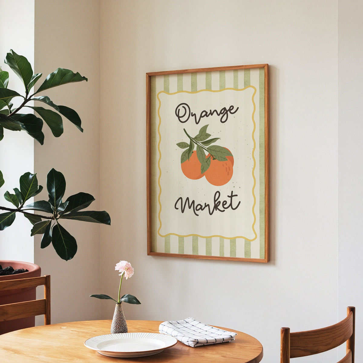 Orange Market print in a walnut frame above a round table beside a fiddle-leaf fig