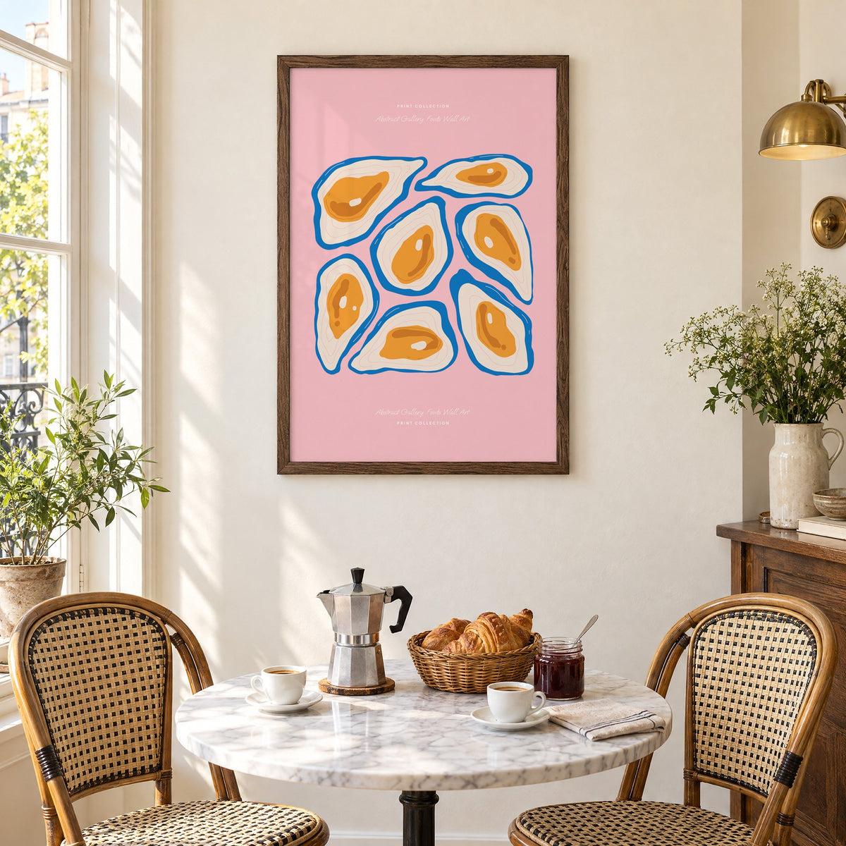 orange oysters blue shells pink print in a walnut frame above a marble bistro table with croissants and rattan chairs