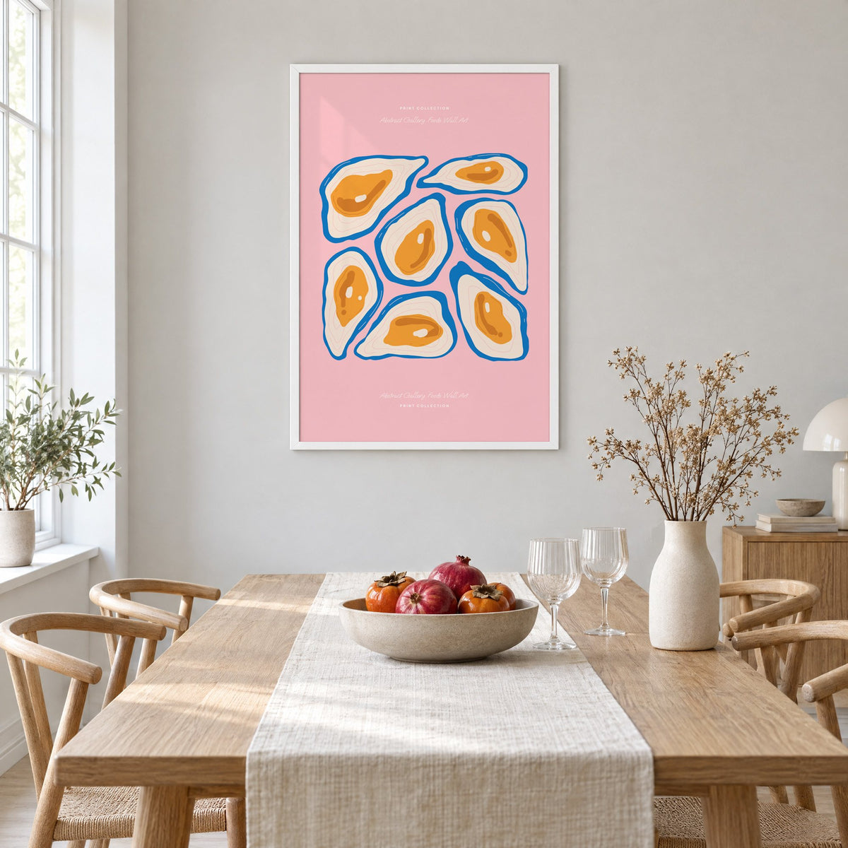 orange oysters blue shells pink print in a white frame above a light oak dining table with a linen runner and fruit bowl
