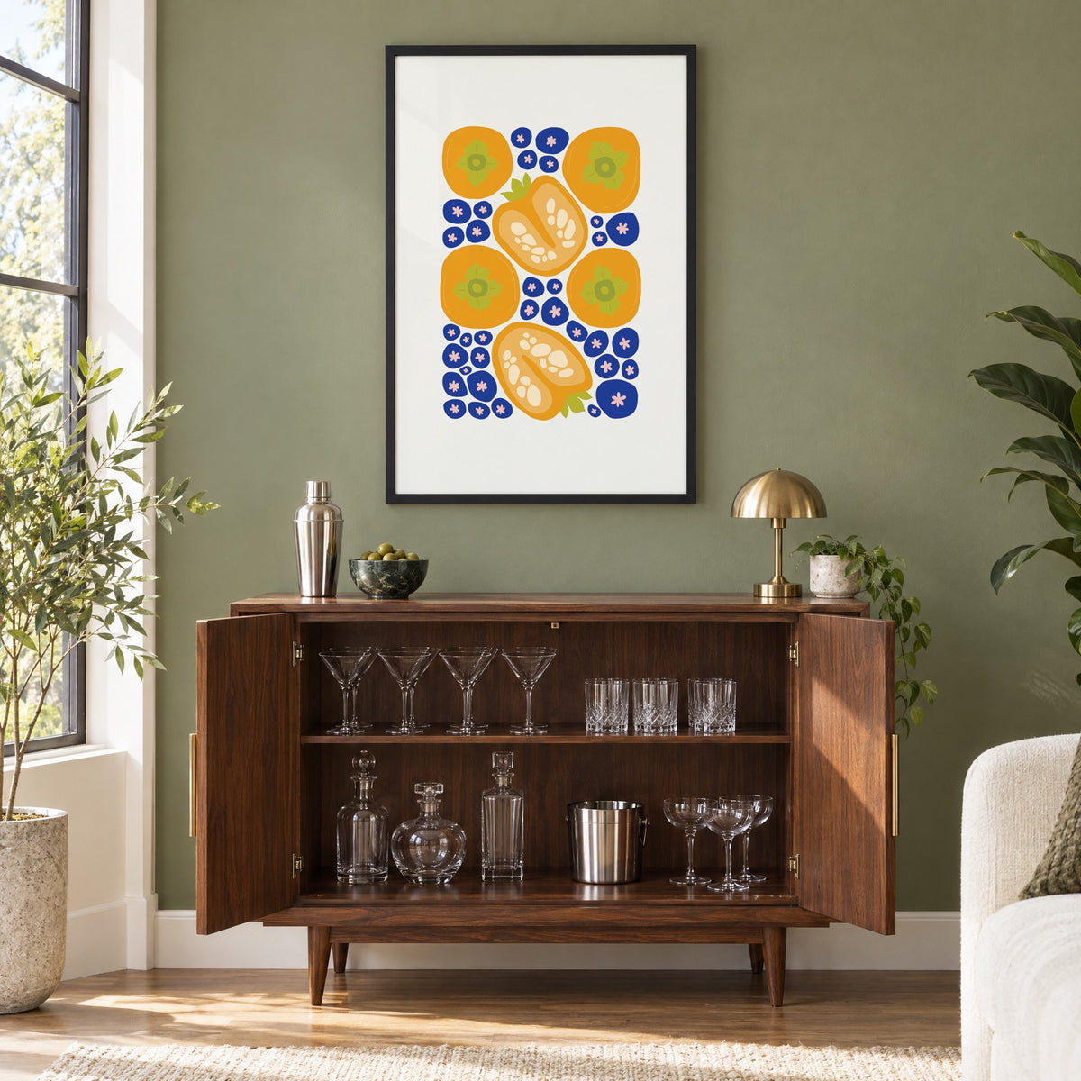 orange persimmons cobalt blueberries pattern print in a black frame on an olive green wall above a walnut bar cabinet with glassware