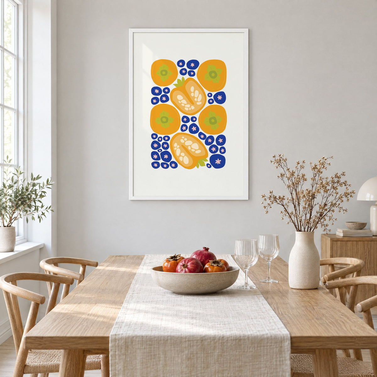 orange persimmons cobalt blueberries pattern print in a white frame above a light oak dining table with a linen runner and fruit bowl