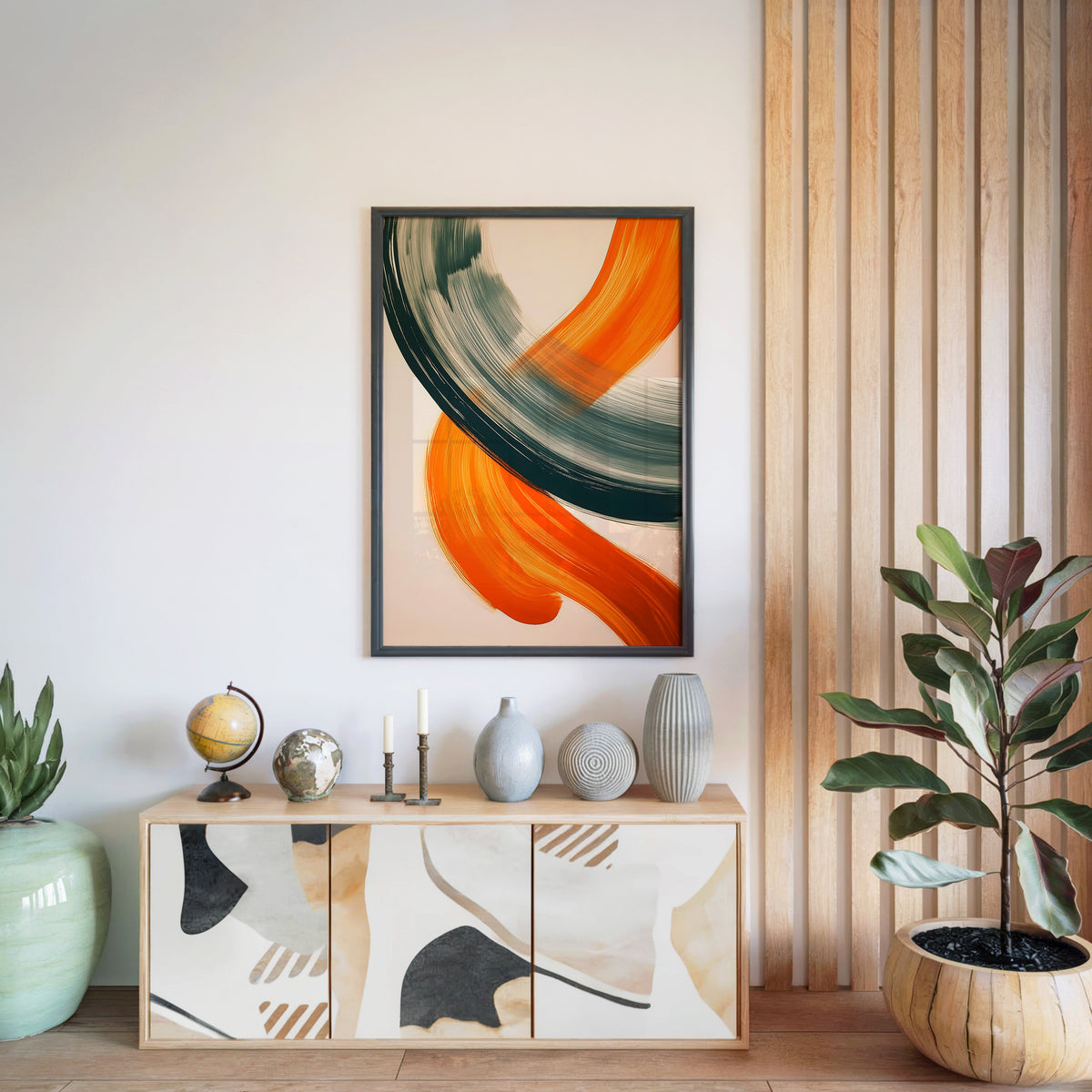 Orange and sage brushstroke arc abstract print in a black frame above a light wood sideboard by a wood slat wall