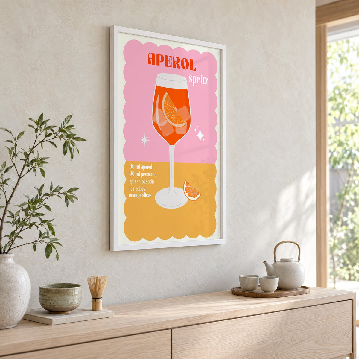 Orange spritz scalloped pink print in a white frame above a pale wood console with a matcha tea set