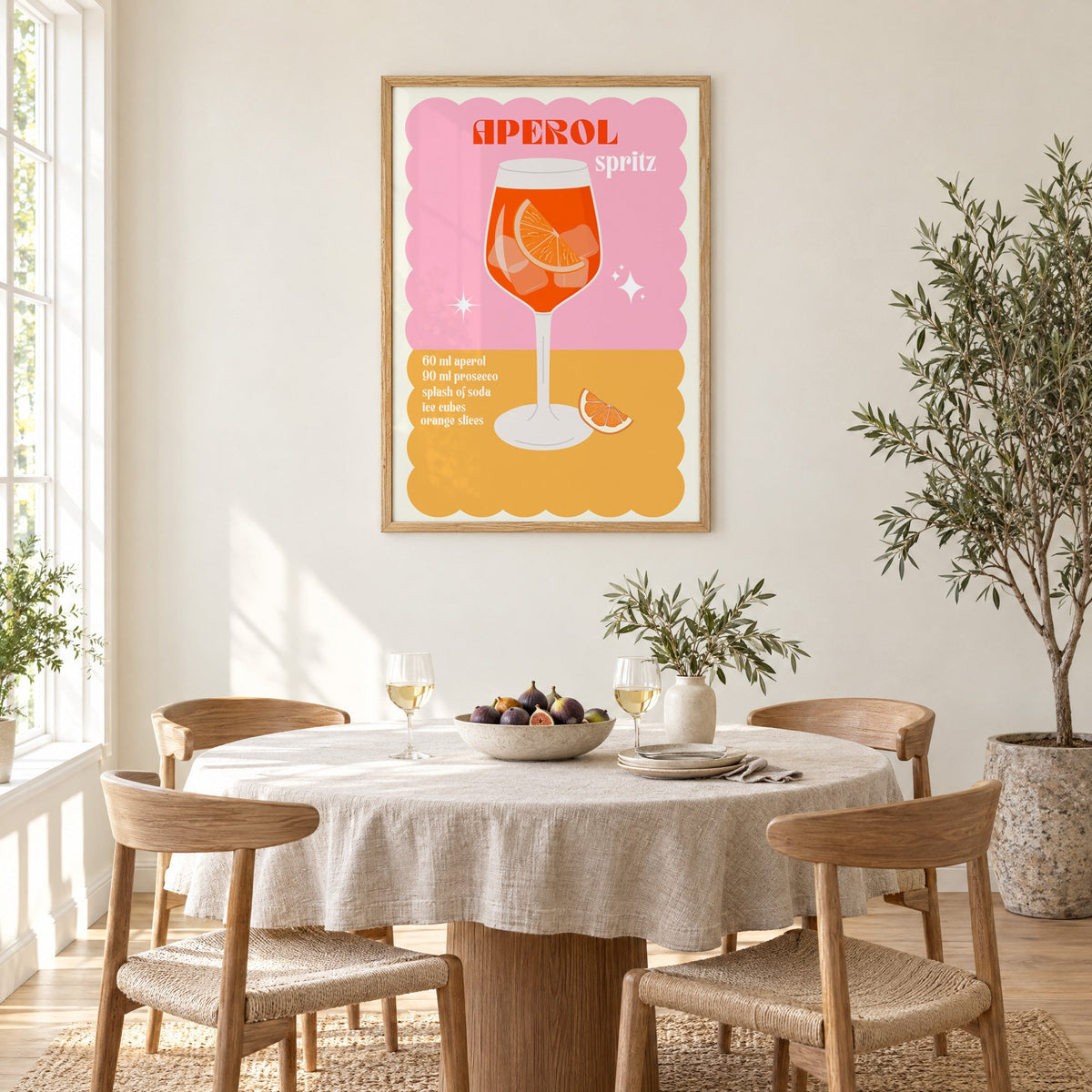 Orange spritz scalloped pink print in an oak frame above a round linen-covered dining table with figs and wine