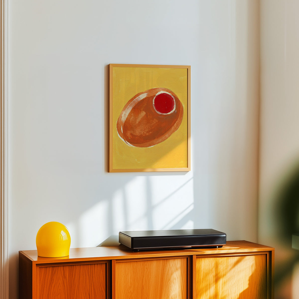 Bar cart olive print in a light oak frame above a teak sideboard with a yellow lamp