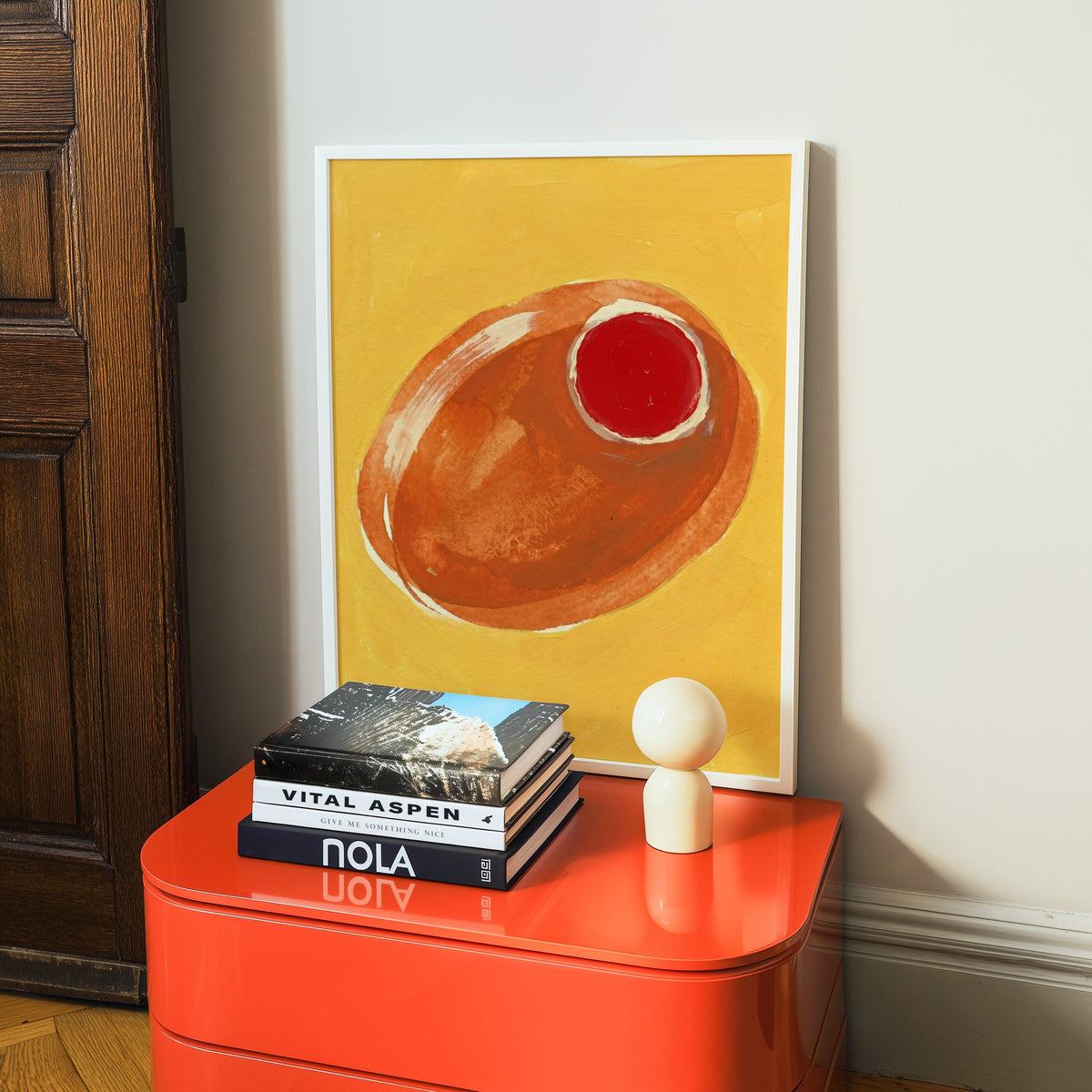 Cocktail olive print in a white frame on a glossy orange cabinet with books
