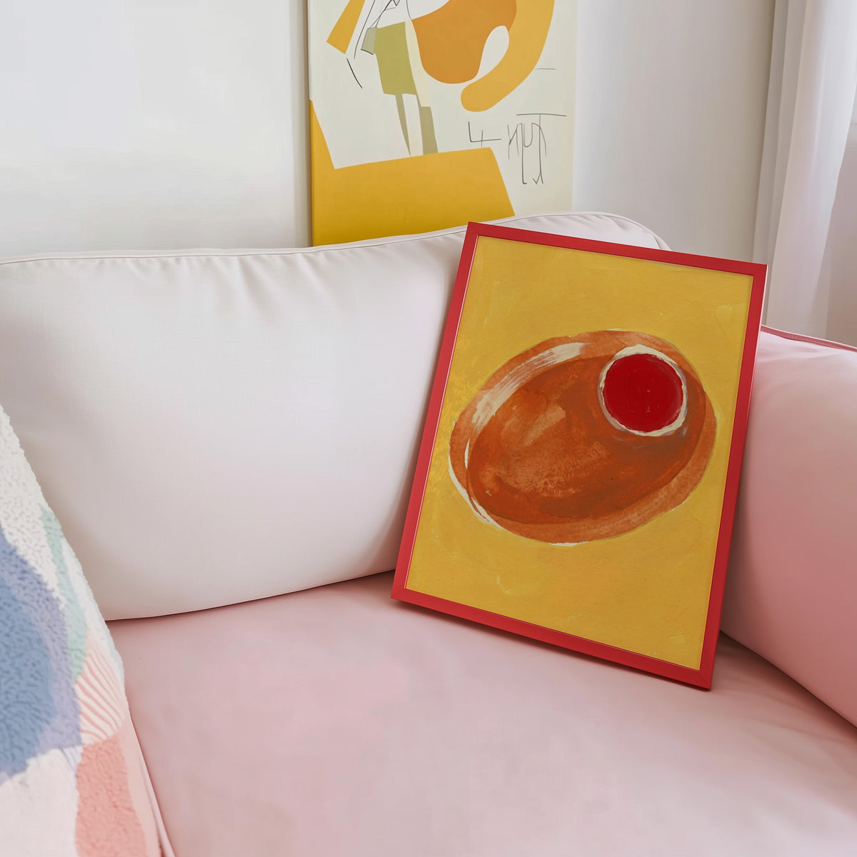 Mustard and orange olive print shown in a red frame leaning on a blush pink sofa
