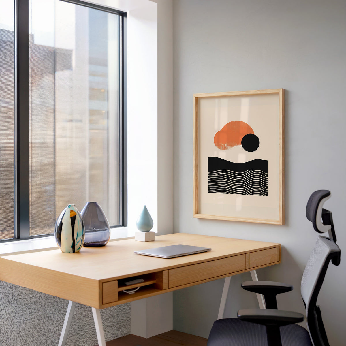 Orange sun and black wave mid century abstract print in a pale wood frame above a home office desk by a tall window