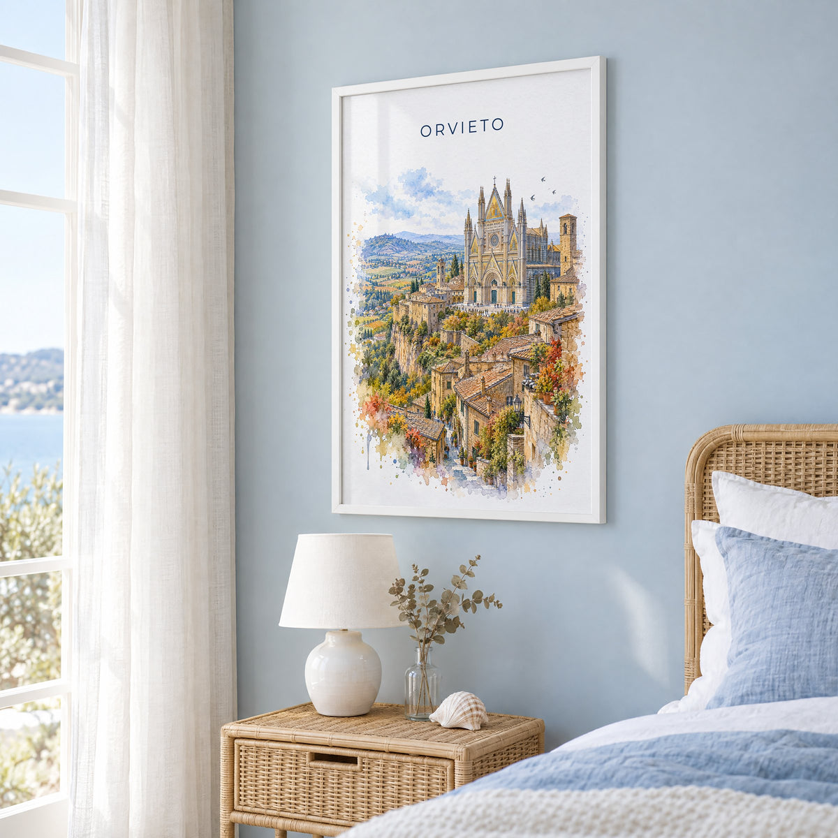 Orvieto watercolor print in a white frame on a pale blue wall beside a rattan bed in a coastal bedroom