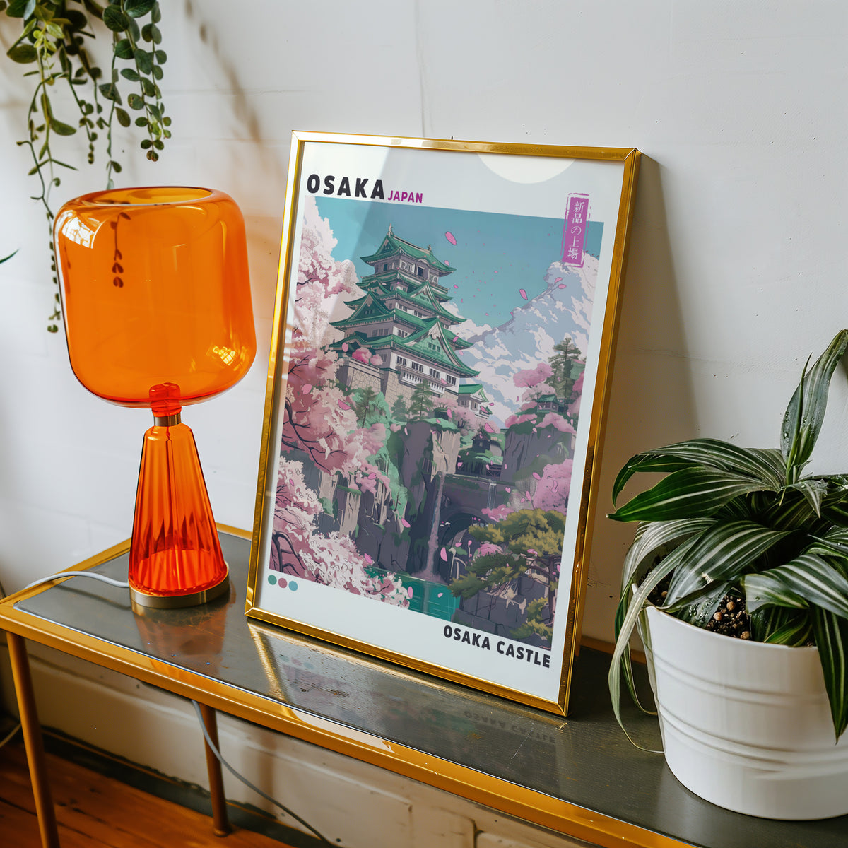 Osaka Castle with cherry blossoms print shown in a gold frame on a console beside an orange glass lamp