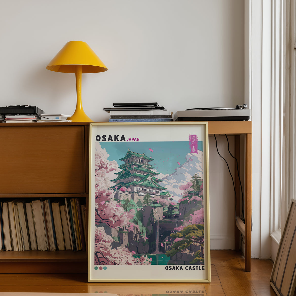 Osaka Castle with cherry blossoms print shown in a gold frame below a teak desk with a yellow lamp