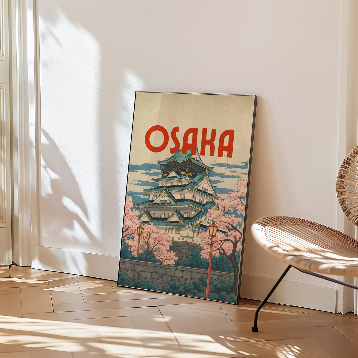 Osaka Castle with teal roofs print in a black frame leaning on a herringbone floor beside a woven rattan chair