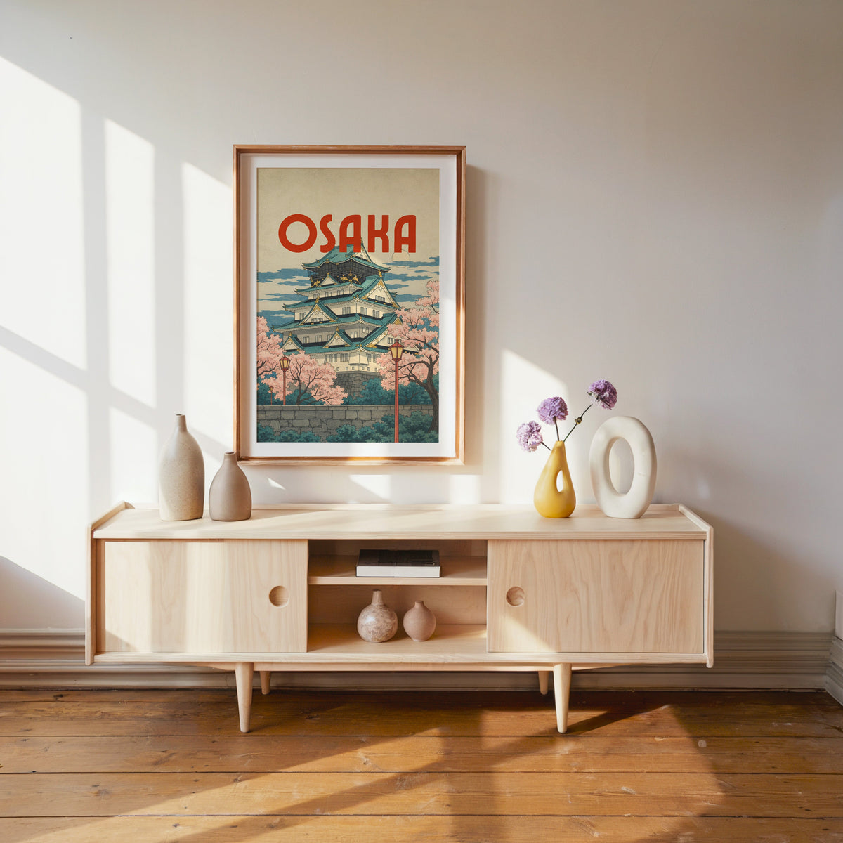 Osaka Castle with teal roofs print shown in a wood frame with a white mat above a pale wood media console