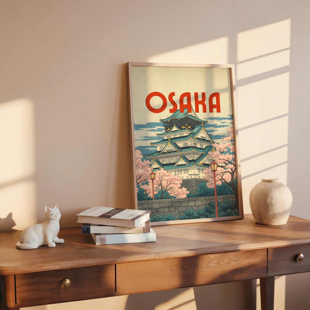 Osaka Castle with teal roofs print shown in a rose gold frame leaning on a wooden writing desk with books