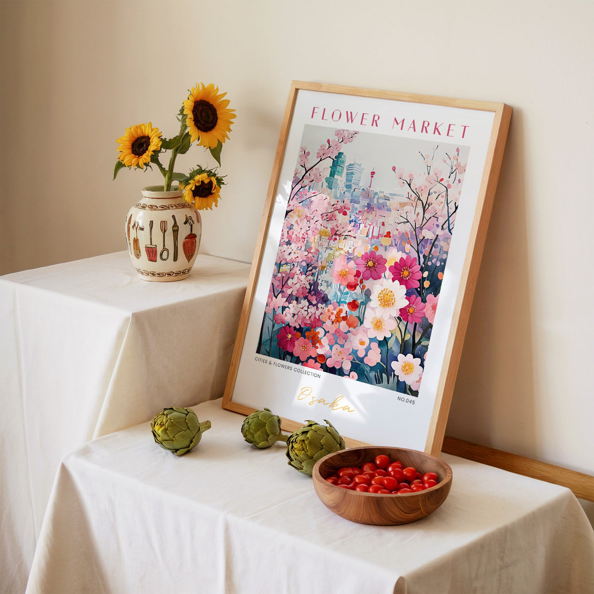 Osaka flower market print in an oak frame leaning on a linen-draped table beside a vase of sunflowers