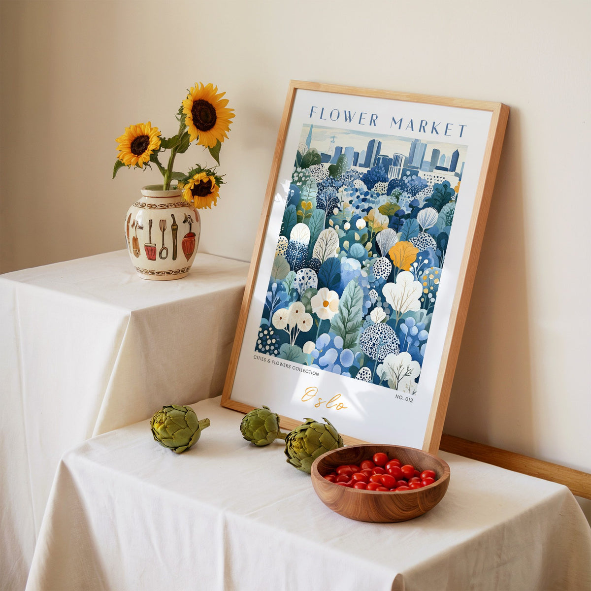 Oslo flower market print in an oak frame leaning on a linen-draped table beside a vase of sunflowers