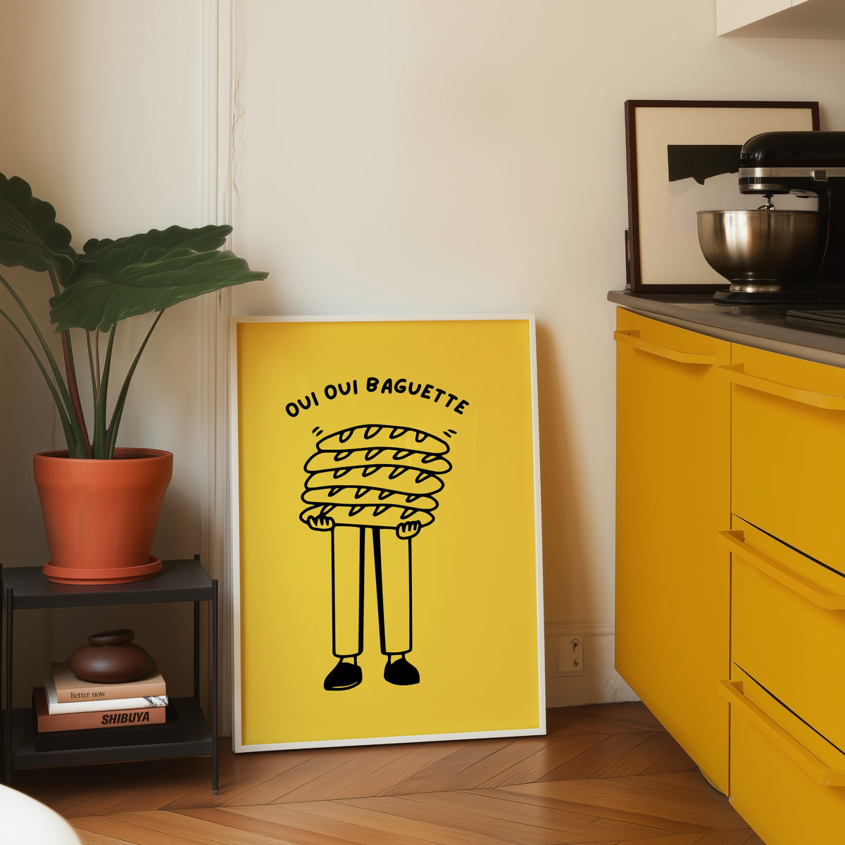 Oui Oui Baguette print in a white frame on parquet beside a bright yellow kitchen