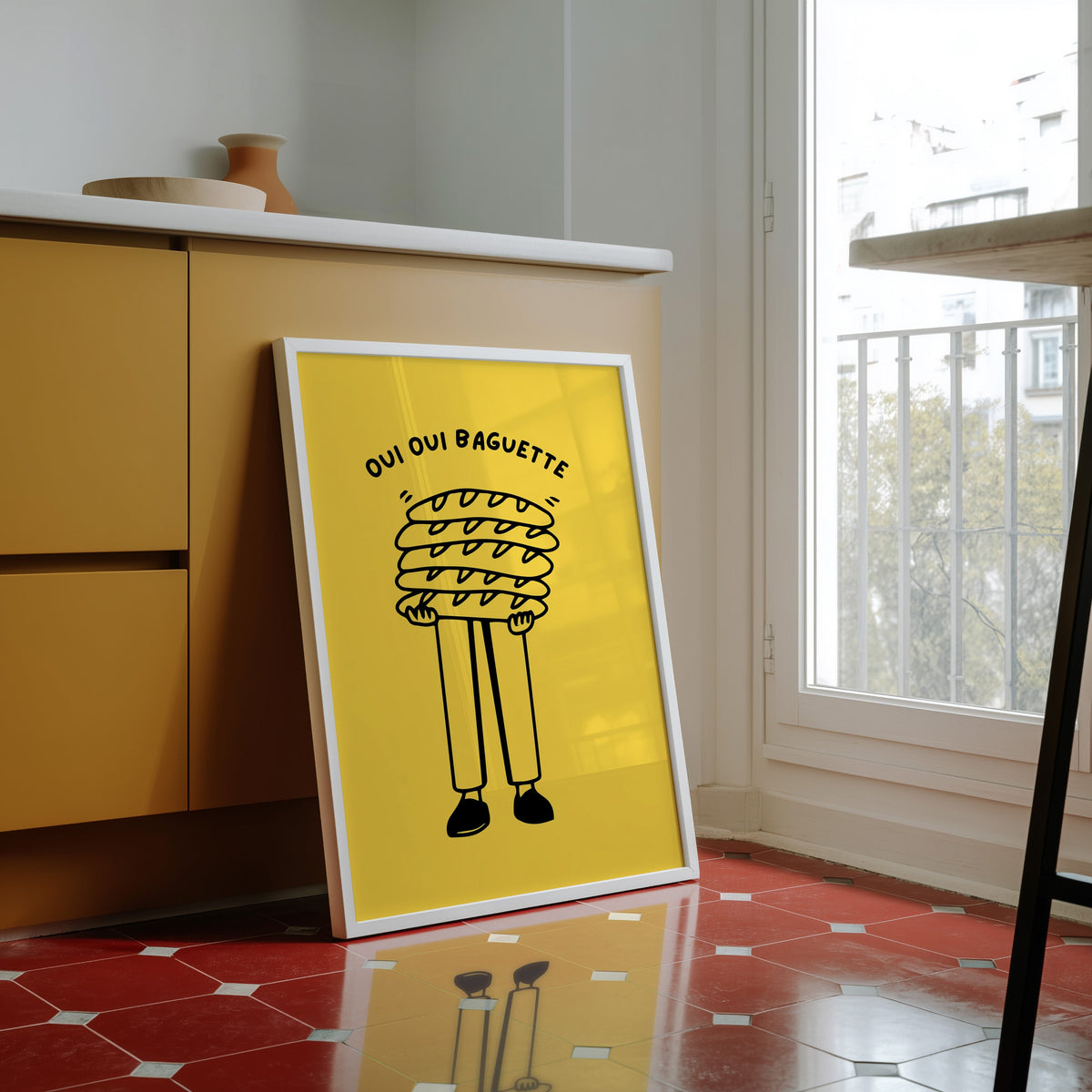 Oui Oui Baguette print in a white frame against yellow cabinets on red tiles