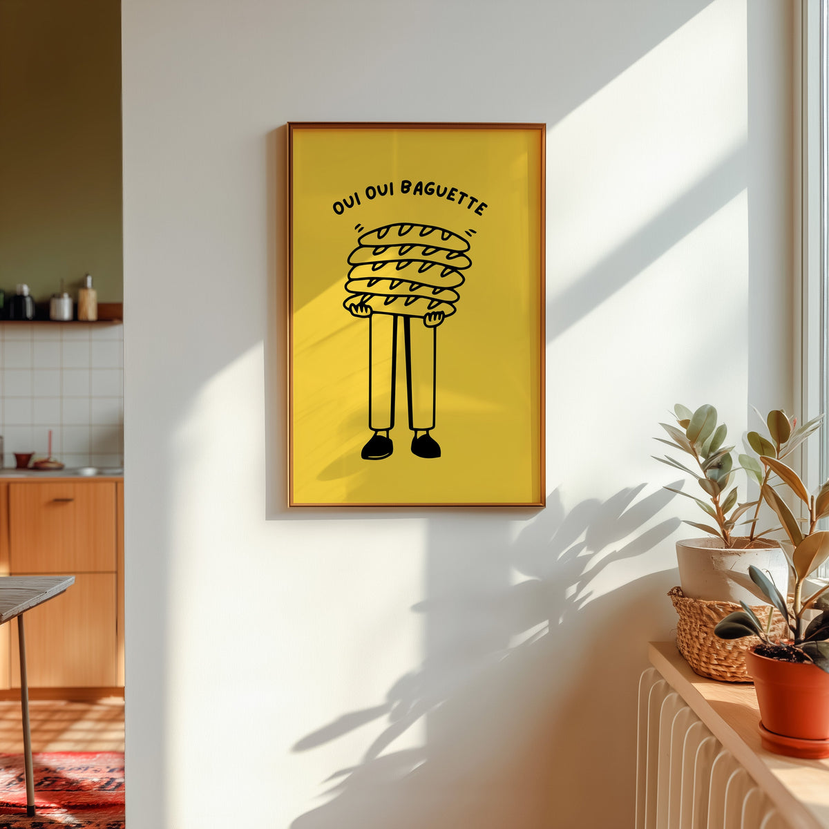 Oui Oui Baguette print in a gold frame in sunlight with plants and a kitchen beyond