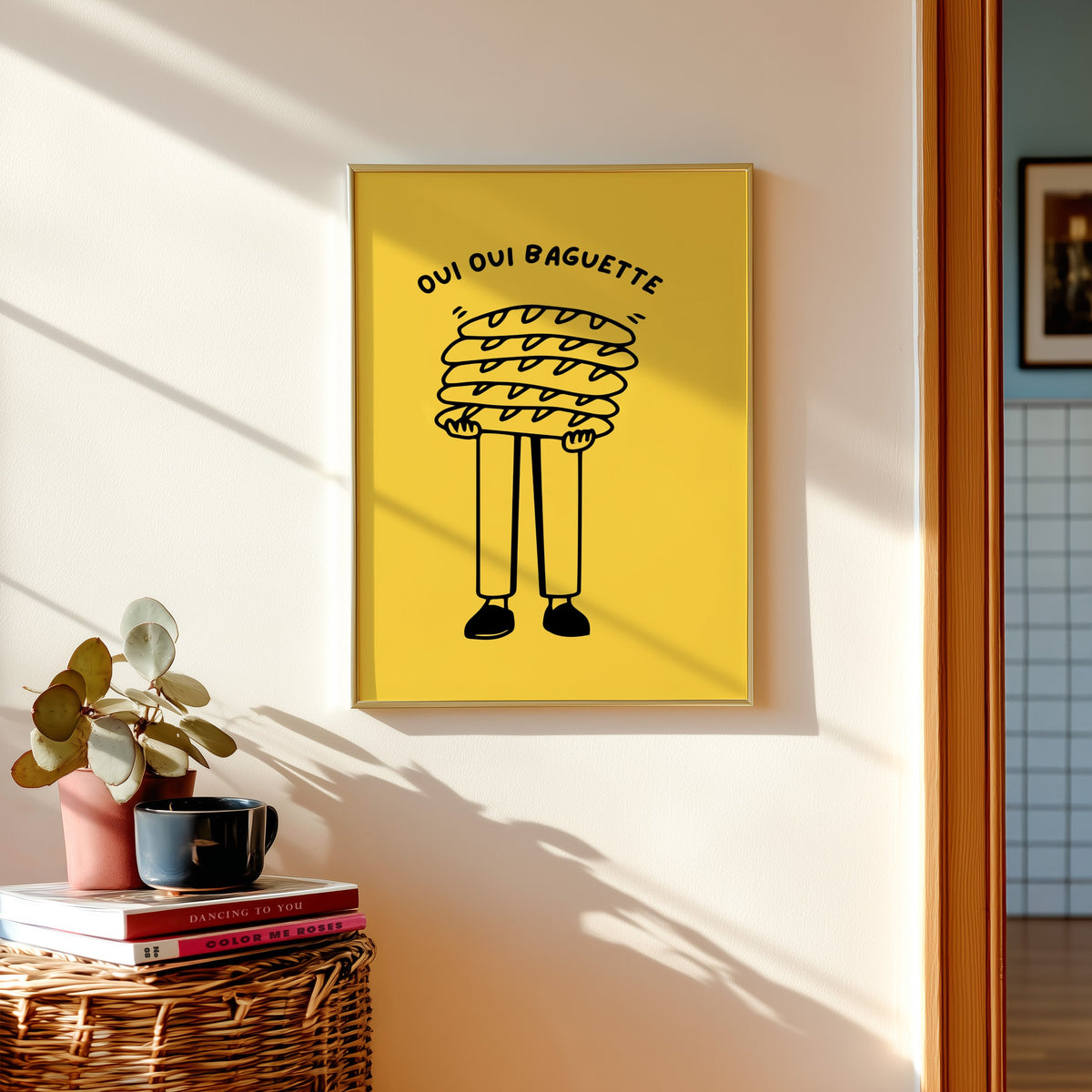 Oui Oui Baguette print in a gold frame above a basket of books and a pilea plant