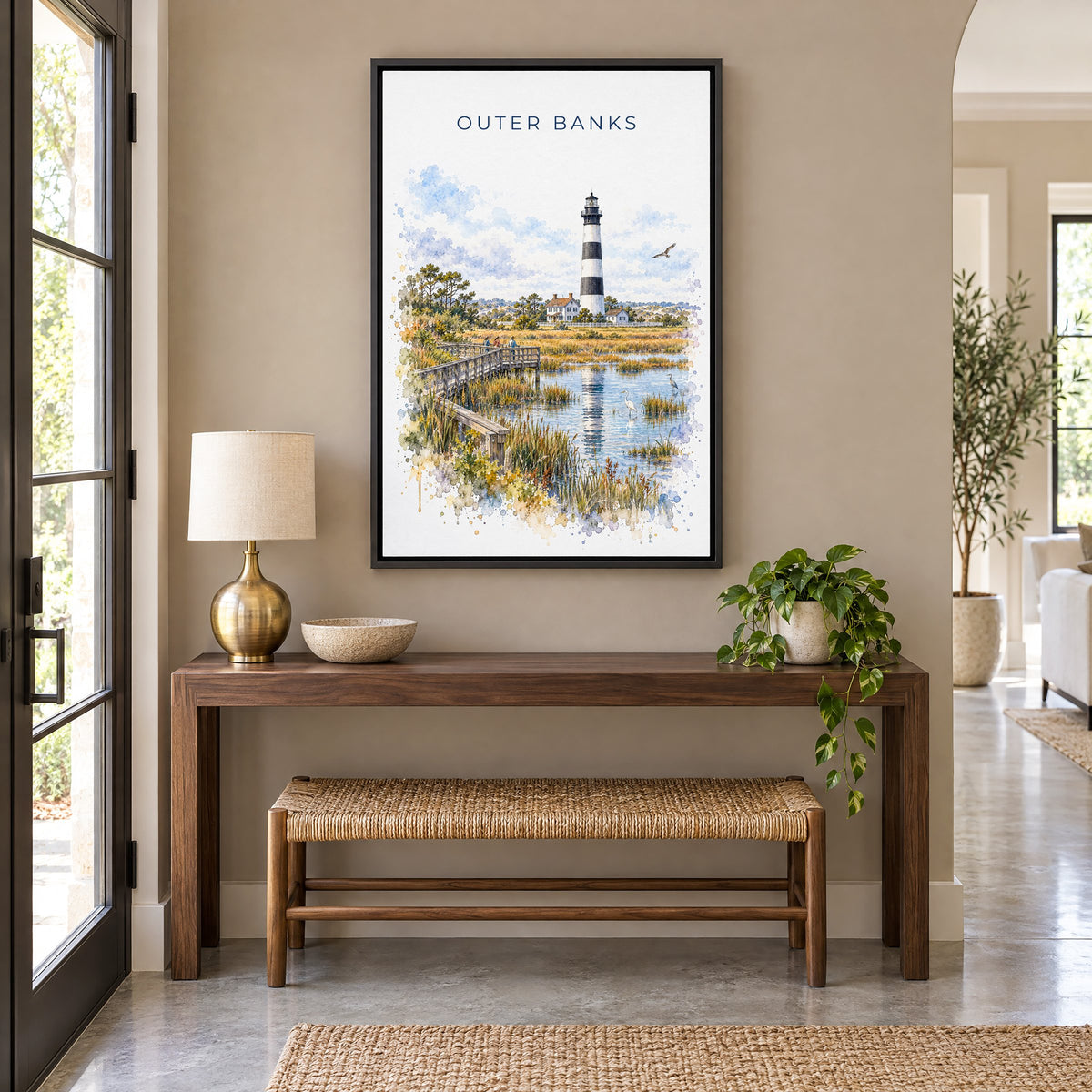 Outer Banks watercolor print as a black floater canvas above a walnut console and woven bench in an entryway