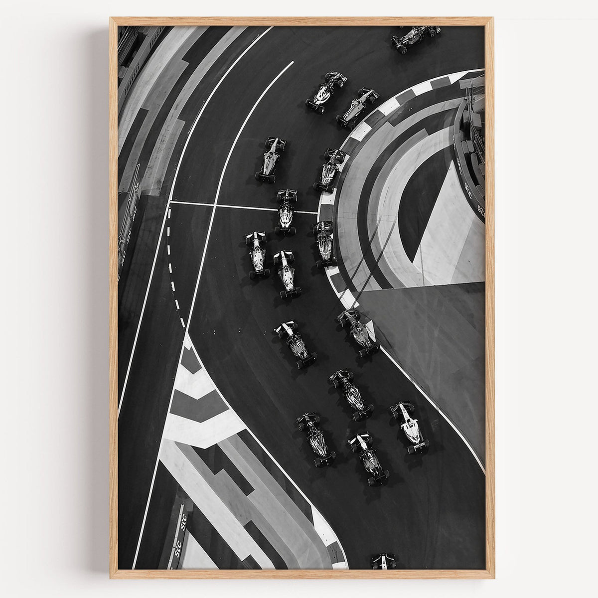 Formula-style race cars on curved track from above print in a light oak frame on a plain white wall