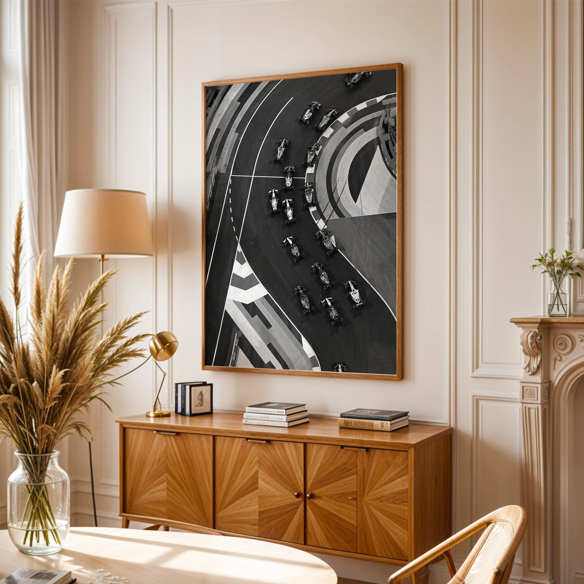 Formula-style race cars on curved track from above print in an oak frame above a sunburst wood sideboard with pampas grass