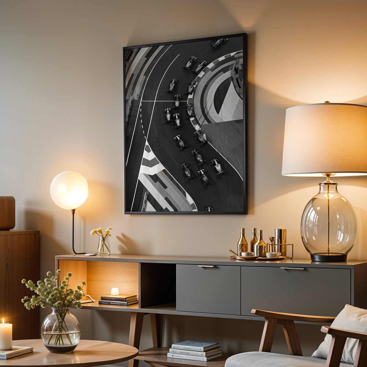 Formula-style race cars on curved track from above print in a black frame above a grey media console with a glass table lamp