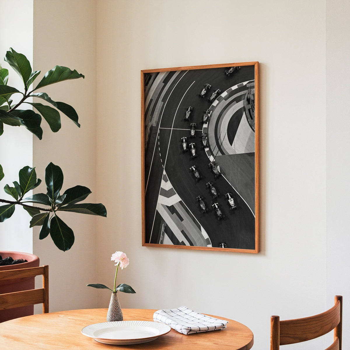Formula-style race cars on curved track from above print in a teak frame above a round wooden dining table