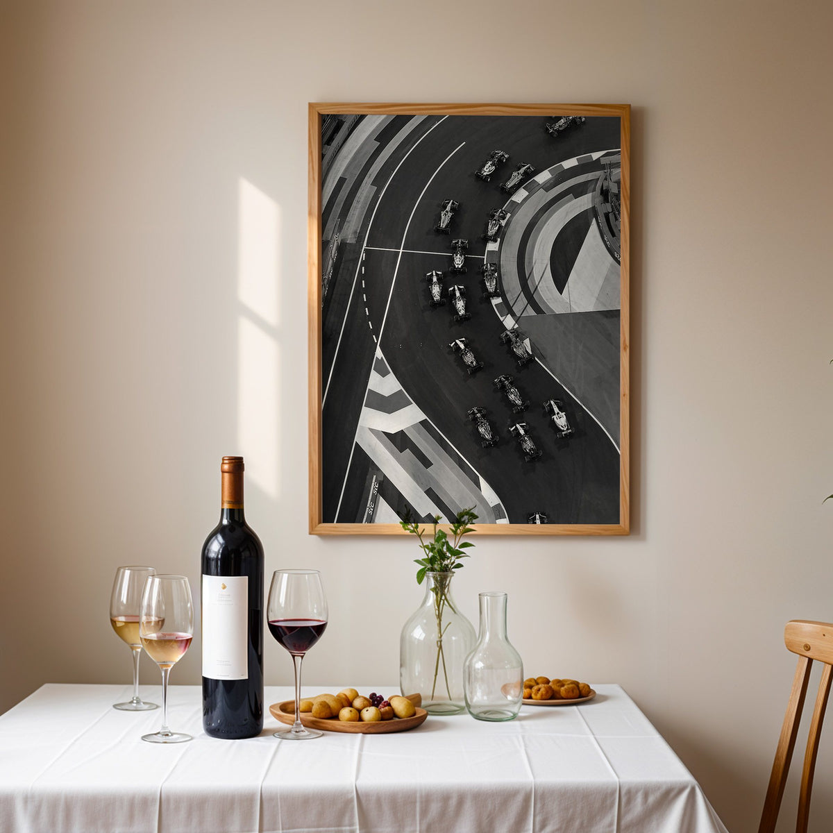 Formula-style race cars on curved track from above print in an oak frame above a table set with red wine and glasses
