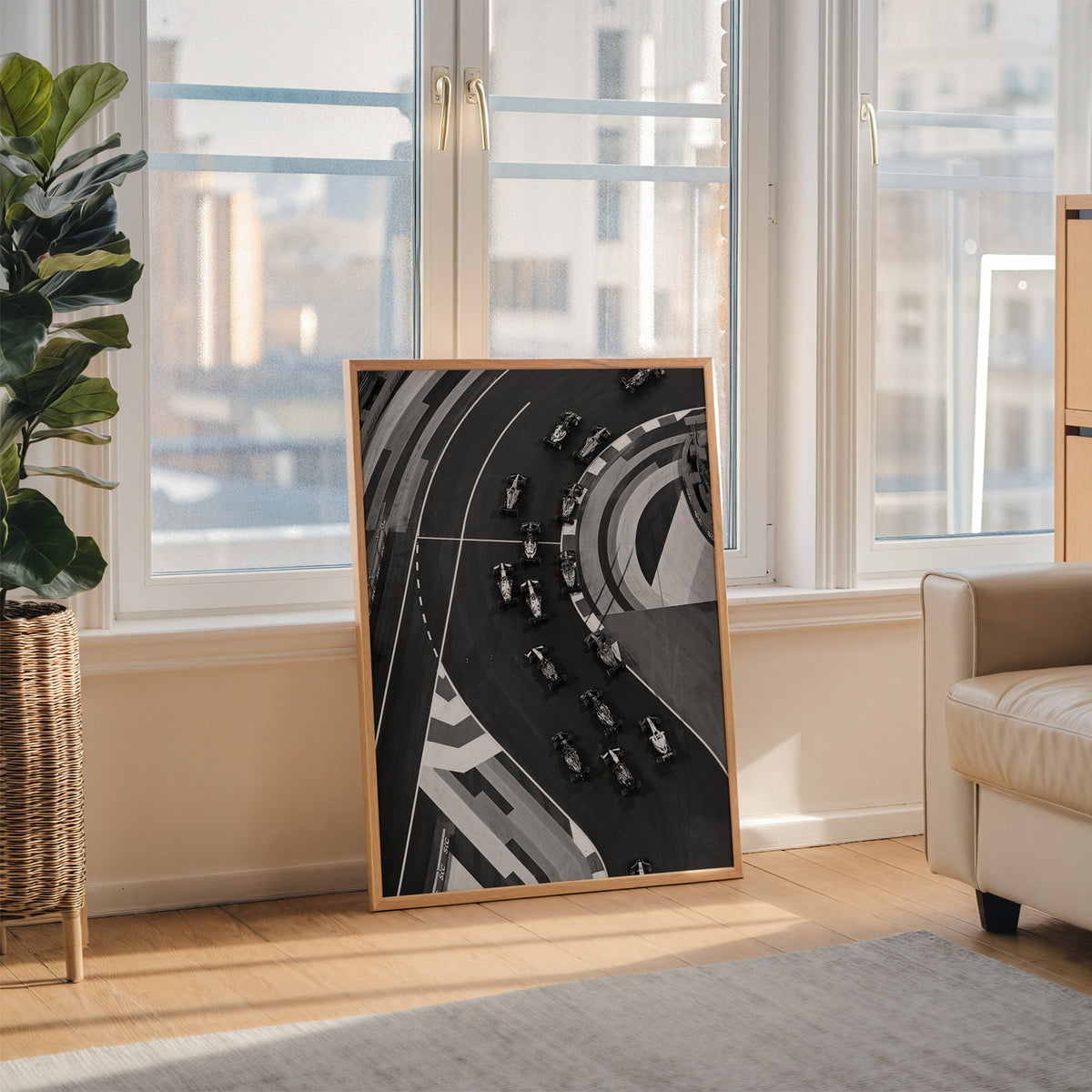 Formula-style race cars on curved track from above print in an oak frame leaning on the floor beside a fiddle leaf fig