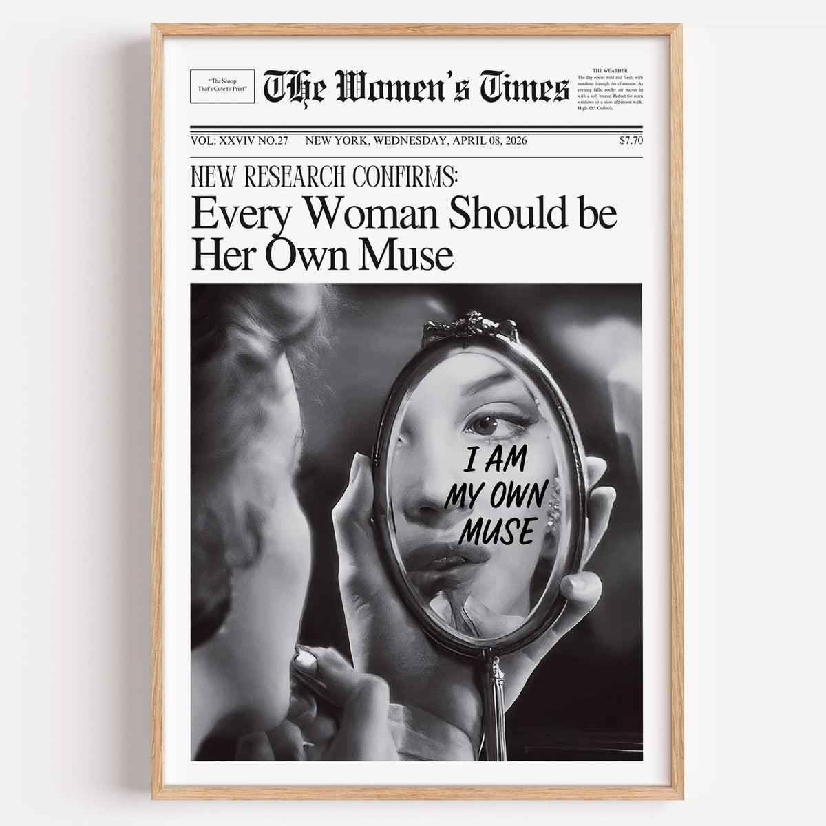 Hand mirror with I am my own muse handwriting print in a light oak frame on a plain white wall