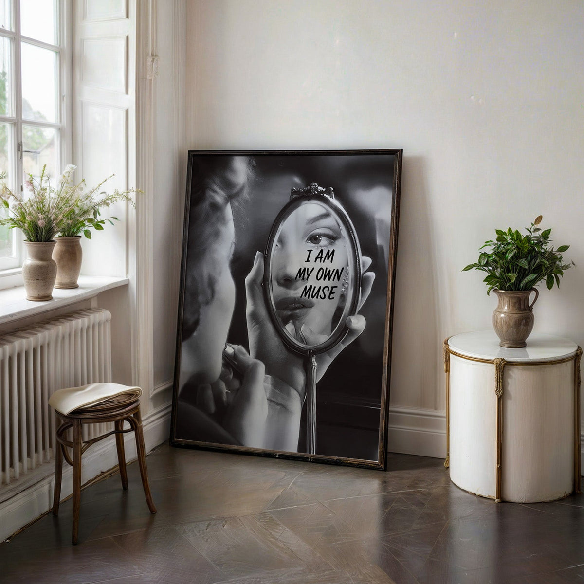 I am my own muse hand mirror portrait print in a black frame on a dark stone floor beside a white side table