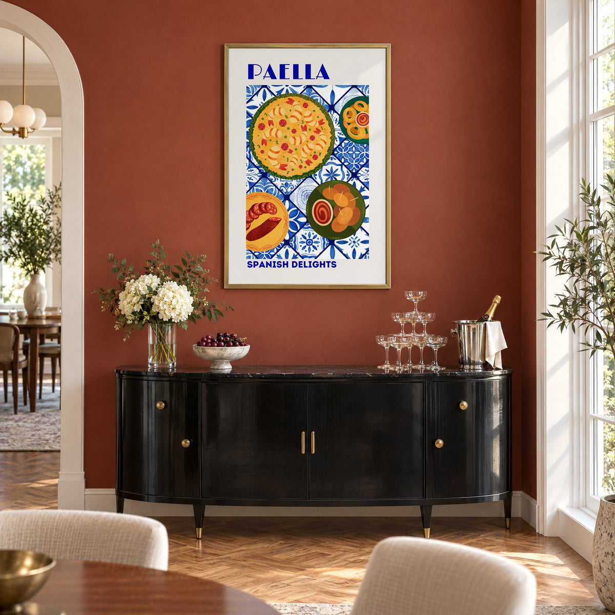 PAELLA Spanish Delights blue tile print in a brass frame on a terracotta wall above a black buffet with a champagne tower